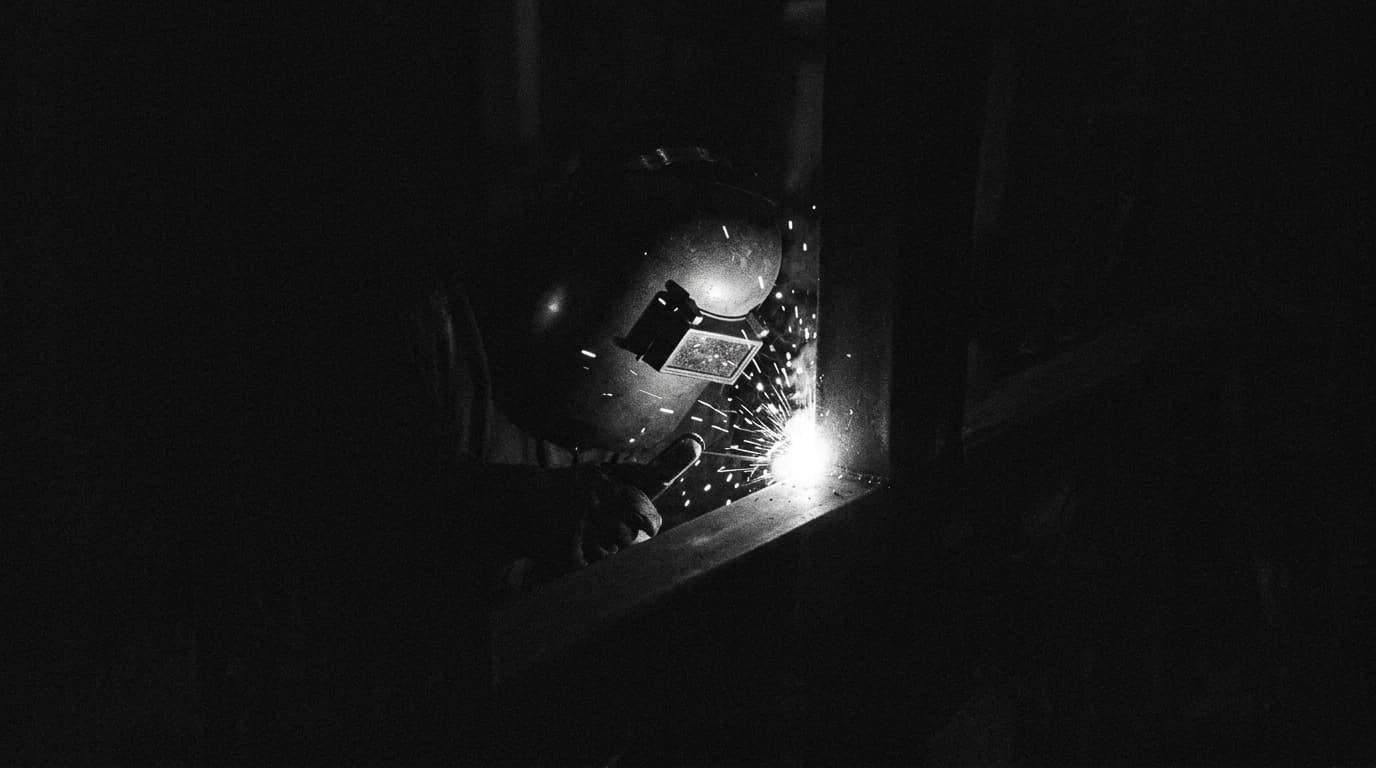 Máscara de soldador iluminada por faíscas na escuridão, representando um trabalhador da construção civil